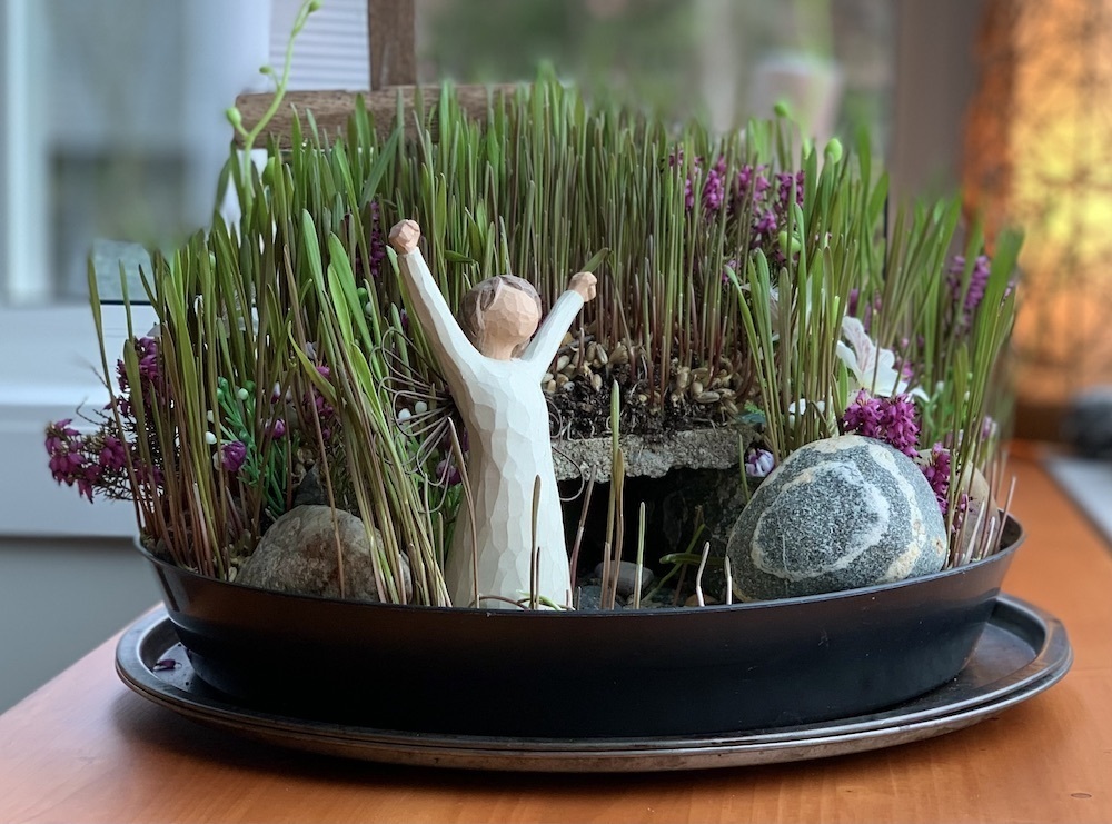 A miniature Easter garden with rye grass sprouting above an empty tomb with the stone rolled away.