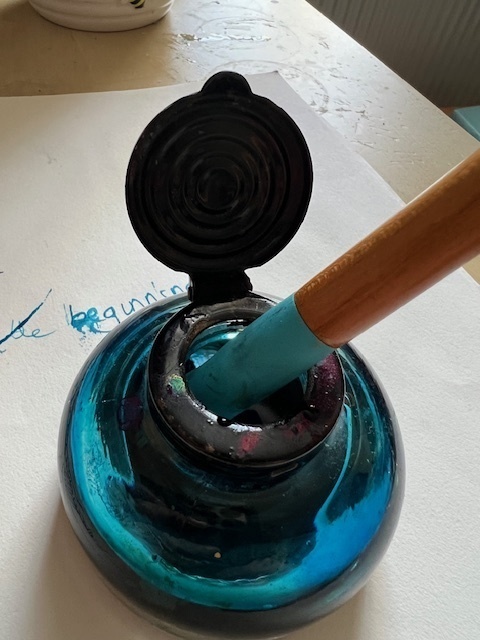 A photograph of an inkwell and dip pen and doodle in turqoise ink